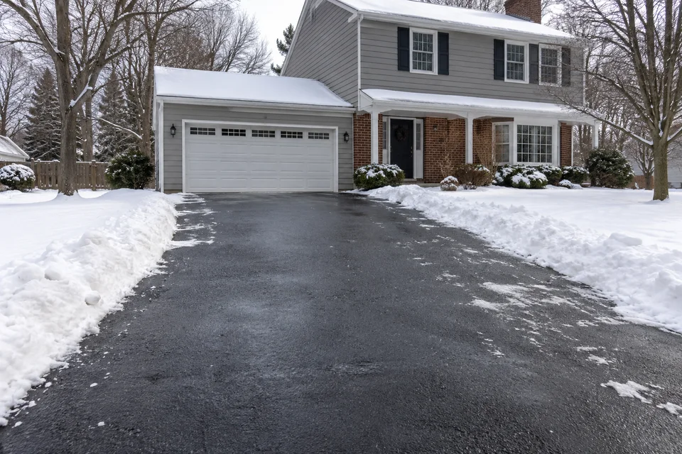 Cleared asphalt driveway bordered by snowbanks beside a two-story home